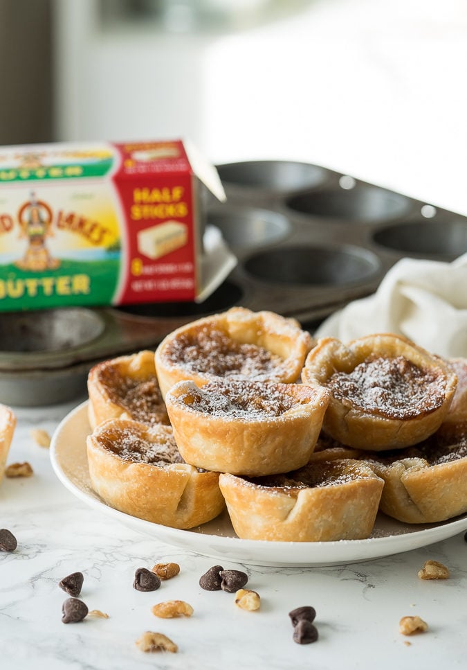 These delicious Chocolate Butter Tarts are filled with walnuts and topped with powdered sugar.